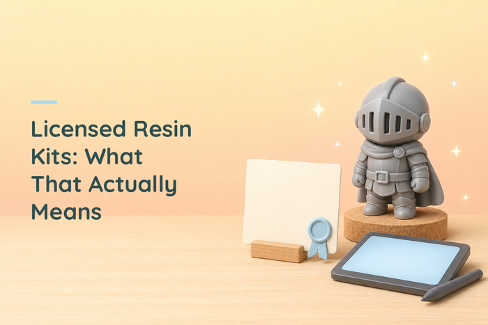 Unpainted grey chibi knight figure on a cork disc beside a blank cream certificate card held in a wooden stand with a light blue rosette seal, and a graphics tablet with a stylus resting on it