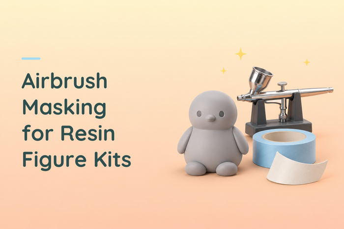 Grey resin bird figure beside an airbrush and blue masking tape