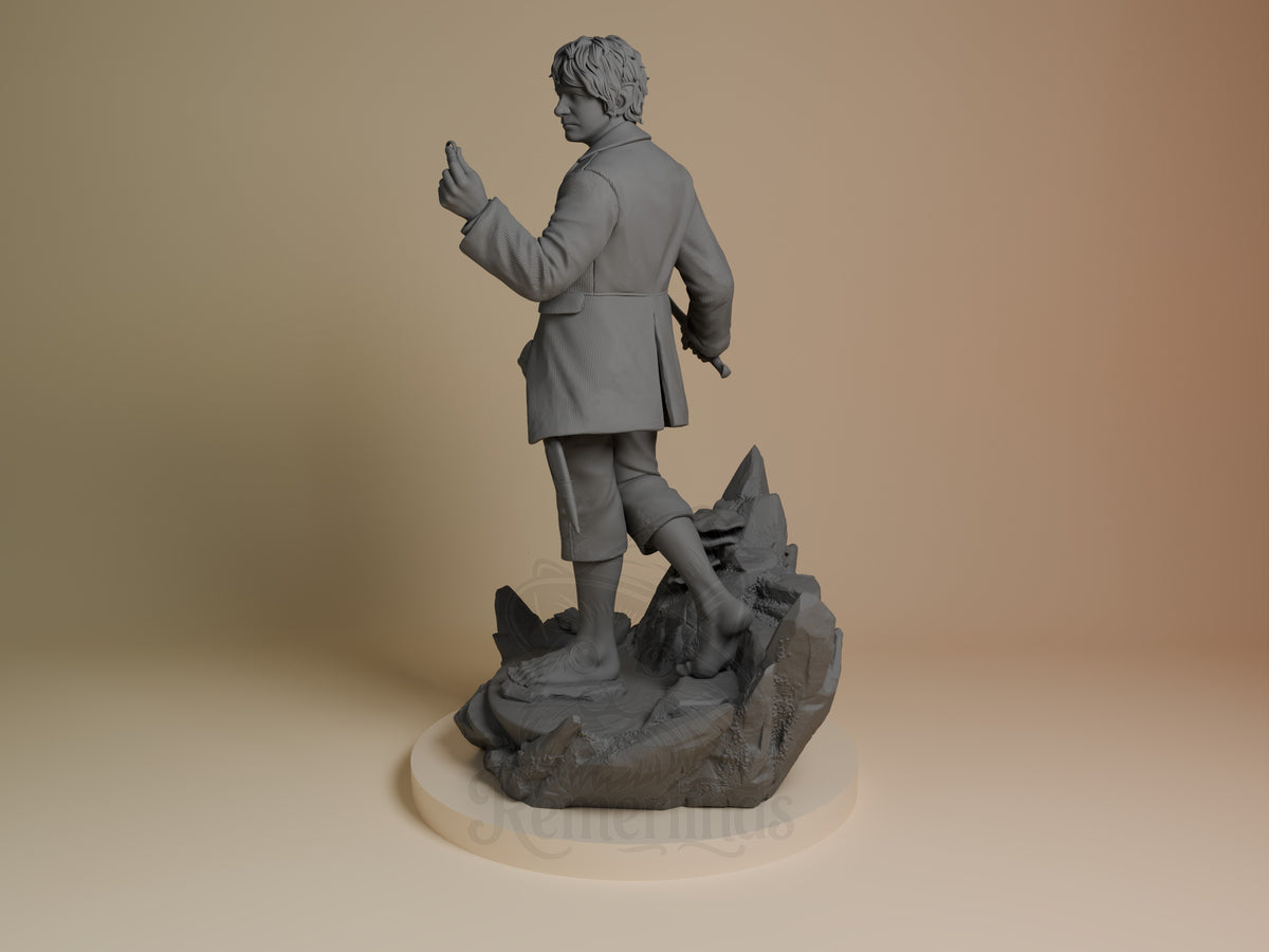 Unpainted resin figure of Bilbo Baggins from Lord of the Rings, viewed from behind on a rocky base.